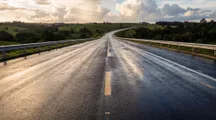 Rodovia de pista dupla molhada, com o horizonte ao entardecer.
