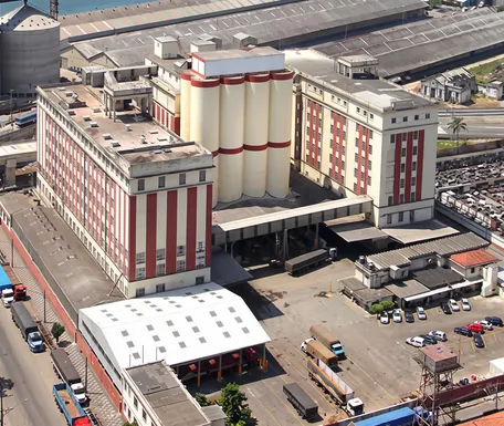 Vista aérea da fábrica da Nita no Porto de Santos, com os prédios listrados de branco e vermelho, os silos e o pátio de caminhões