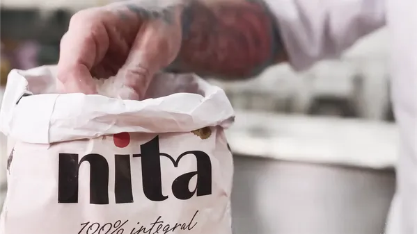 Mão pegando farinha de dentro de um saco de papel da Nita, de farinha 100% integral
