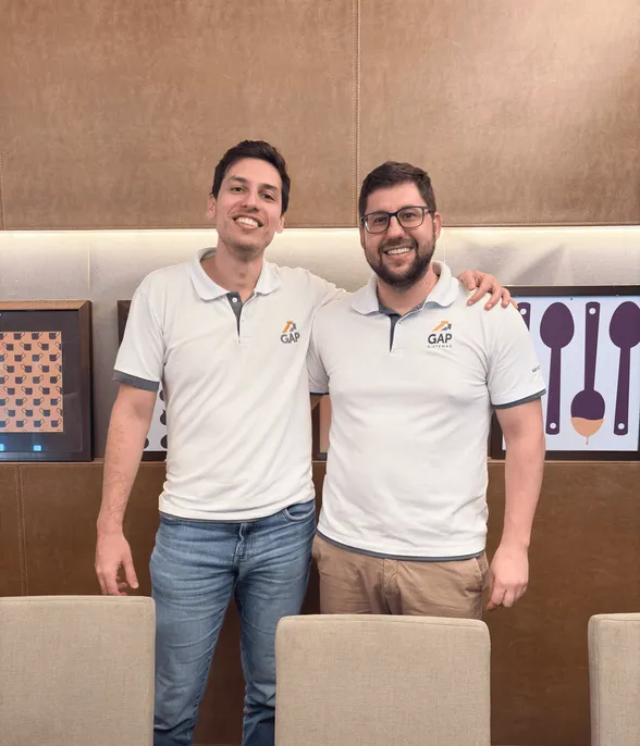 Cuatro miembros del equipo de GAP Sistemas, vistiendo polos blancos con el logo, sonriendo y posando en el stand de la empresa en un evento, con el logo de GAP al fondo.
