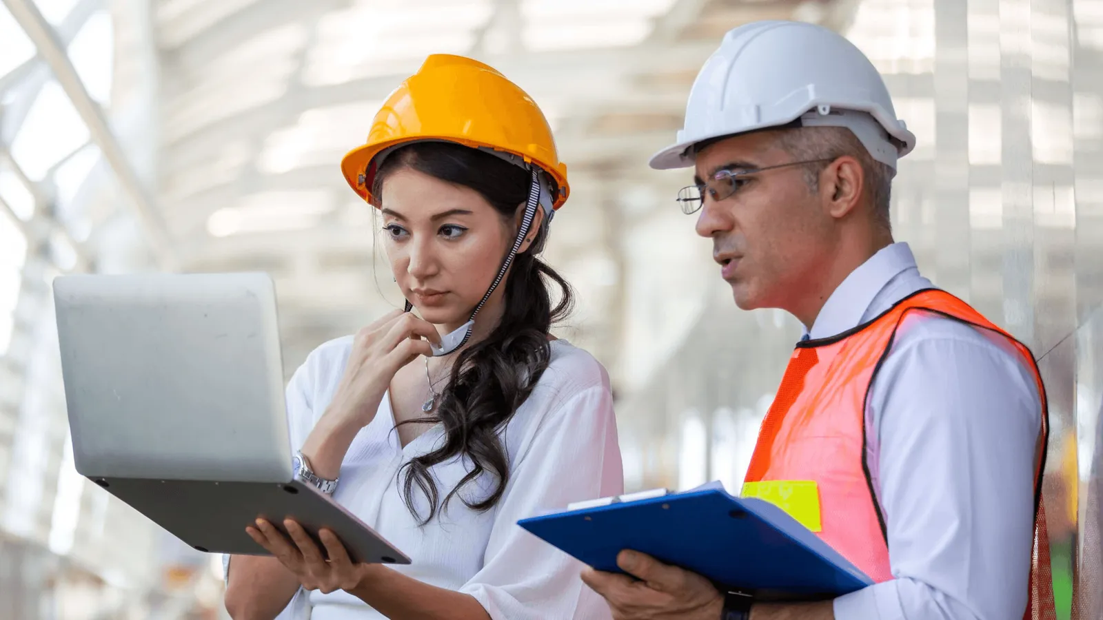 Dos profesionales con casco analizan una computadora portátil en un área industrial.